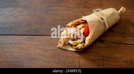 Gyro pita Shawarma su tavola di legno. Cibo greco, affettati, patate, pomodori e tzatziki, impacco di carta, vista dall'alto. Foto Stock