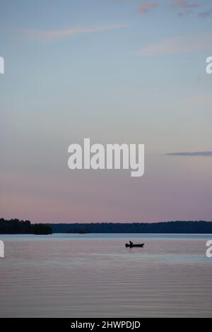 Un uomo in una piccola barca su un lago tranquillo al tramonto Foto Stock