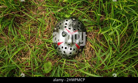 La maschera di hockey in plastica creepy di colore metallico si trova sul terreno Foto Stock