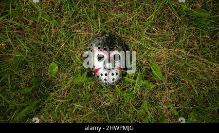 La maschera di hockey in plastica creepy di colore metallico si trova sul terreno Foto Stock