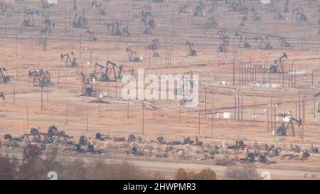 Pozzi con martinetti a pompa su campo di petrolio, California USA. Carri per estrazione fossile grezza che lavorano su giacimenti petroliferi. Paesaggio industriale, derricks nella valle del deserto. Molti pumpjacks piattaforme su oilpozzi pompando. Foto Stock