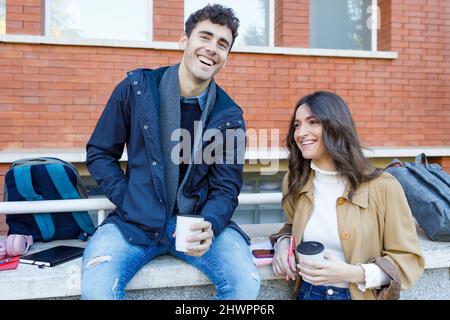 Amici allegri con tazza usa e getta nel campus universitario Foto Stock