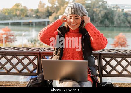 Donna felice seduta con laptop che regola le cuffie intrauricolari Foto Stock