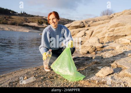 Sorridente volontario che raccoglie una bottiglia di plastica al mare Foto Stock