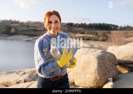 Sorridente volontario che tiene bottiglie di plastica in spiaggia Foto Stock