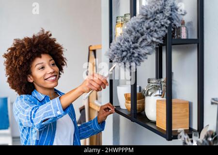 Sorridente giovane donna che pulisce rack in cucina a casa Foto Stock
