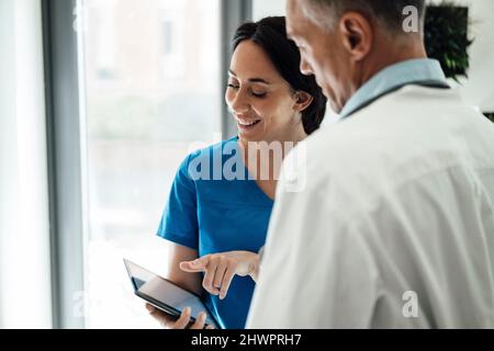 Infermiera sorridente che parla con il medico sopra il tablet PC in ospedale Foto Stock
