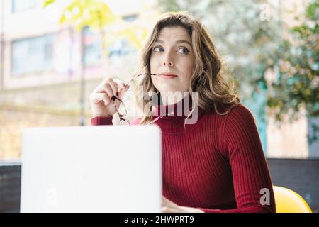 Donna premurosa con computer portatile nel caffè sul marciapiede Foto Stock