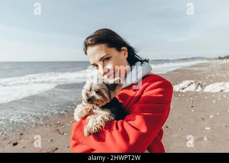 Donna sorridente che porta il terrier dello Yorkshire in spiaggia Foto Stock