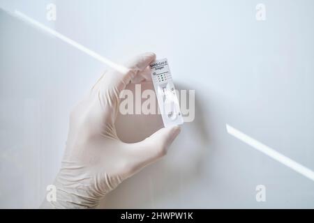 Dispositivo diagnostico rapido con supporto manuale che mostra risultati positivi COVID-19 su sfondo bianco Foto Stock