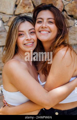 Sorridenti giovani donne che si abbracciano davanti al muro Foto Stock