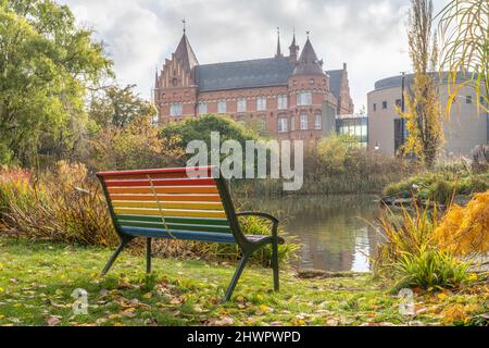 Svezia, Skane County, Malmo, panca color arcobaleno di fronte al parco stagno con Malmo City Library sullo sfondo Foto Stock