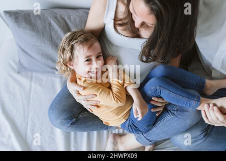 Ragazza allegra sdraiata sul grembo della madre incinta a casa Foto Stock