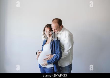 Uomo che abbraccia donna incinta felice da parete Foto Stock
