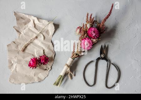 Studio shot of scissors, piece of paper and small bouquet of dried flowers Foto Stock