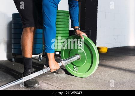 Atleta mettere le piastre di peso in barbell prima di esercitarsi in palestra Foto Stock