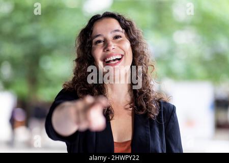 Giovane donna d'affari con capelli marroni ricci ridendo Foto Stock
