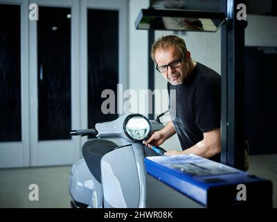 Meccanico che regola il faro sullo scooter a motore presso l'officina di riparazione auto Foto Stock