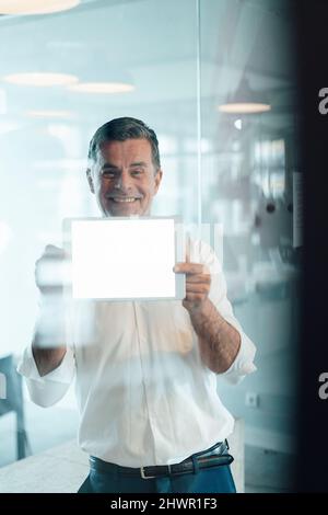 Uomo d'affari sorridente che mostra uno schermo vuoto del tablet PC in ufficio Foto Stock