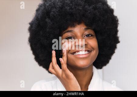 Sorridente Afro donna applicazione crema viso Foto Stock