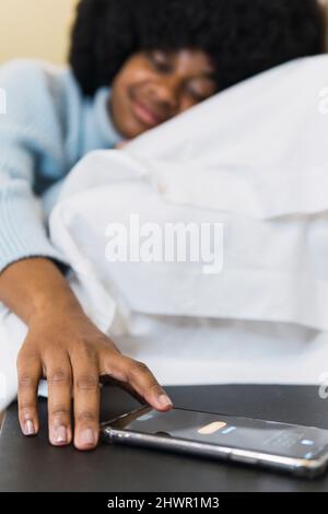 Donna che spegne la sveglia sullo smartphone in camera da letto a casa Foto Stock