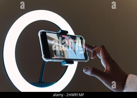 Donna sorridente che vlogging su smartphone in luce anulare illuminata Foto Stock