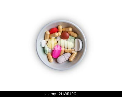 Una ciotola bianca di varie pillole colorate e capsule isolate su sfondo bianco. Foto Stock
