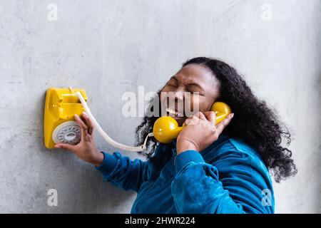 Donna che parla attraverso il ricevitore telefonico vecchio stile ridendo di fronte al muro grigio Foto Stock