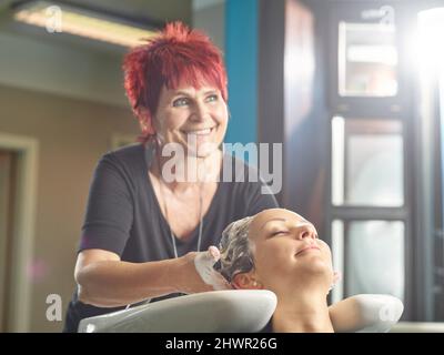 Felice parrucchiere lavaggio capelli donna in salone Foto Stock