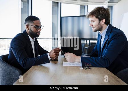 Uomo d'affari che dà la penna al cliente per firmare il contratto in ufficio Foto Stock