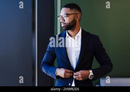 Un uomo d'affari contemplativo che regola il blazer in ufficio Foto Stock