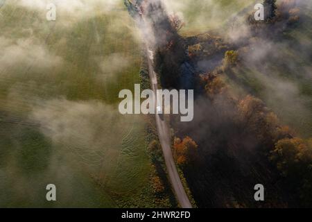 Vista del drone della strada sterrata campagna che si estende lungo il fiume a nebbia mattina d'autunno Foto Stock