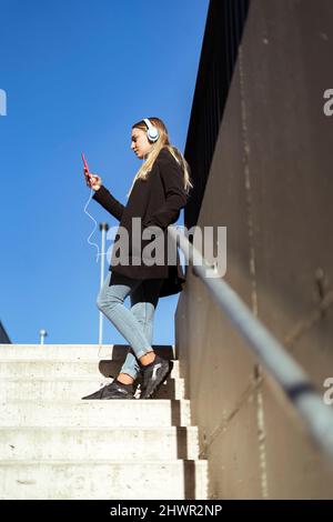 Donna che utilizza il telefono cellulare in piedi su gradini Foto Stock