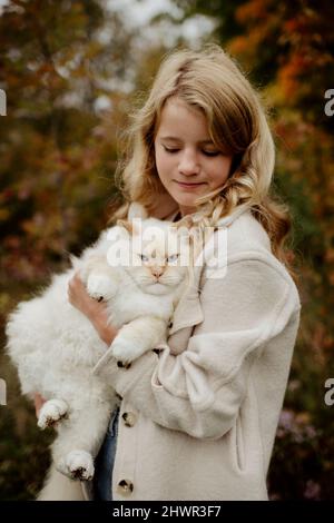 Ragazza bionda che porta Ragdoll gatto in giardino Foto Stock