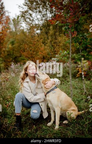 Cane che lecca la faccia della ragazza bionda in giardino Foto Stock