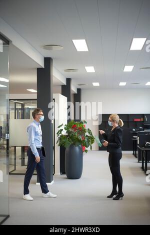 Donna d'affari che parla con un collega e che mantiene la distanza sociale durante le riunioni in ufficio Foto Stock