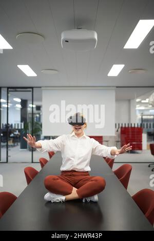 Donna d'affari allegra che indossa occhiali VR seduti nella sala riunioni dell'ufficio Foto Stock
