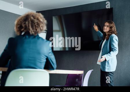 Giovane donna d'affari che presenta al collega nella sala del consiglio di amministrazione Foto Stock