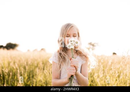 Ragazza carina che odora i fiori margherita in campo Foto Stock