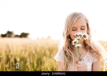 Ragazza bionda che odora i fiori in campo Foto Stock