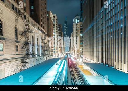 Percorsi leggeri su binari ferroviari tra edifici in città di notte, Chicago, USA Foto Stock