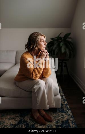 Donna anziana bionda seduta con mano sul mento a casa Foto Stock