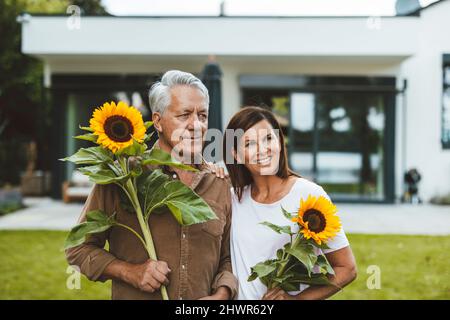 Coppia con girasoli in piedi sul cortile Foto Stock