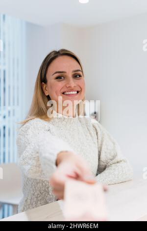 Giovane donna felice al banco di ricevimento in clinica Foto Stock