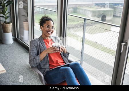 Donna d'affari sorridente con una tazza di caffè sul posto di lavoro Foto Stock