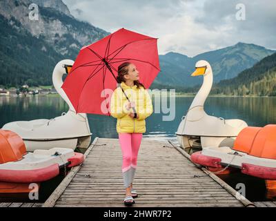 Ragazza con ombrello a piedi da pedalò sul molo Foto Stock