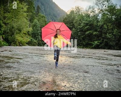 Ragazza felice che tiene l'ombrello e spruzzi d'acqua nel lago Foto Stock