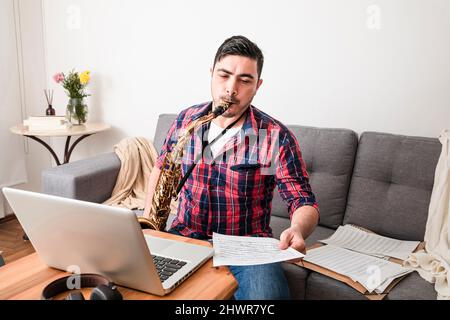 Uomo che suona il sassofono guardando le note musicali nel salotto di casa Foto Stock