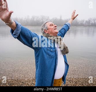 Uomo anziano in piedi con gli occhi chiusi in spiaggia Foto Stock
