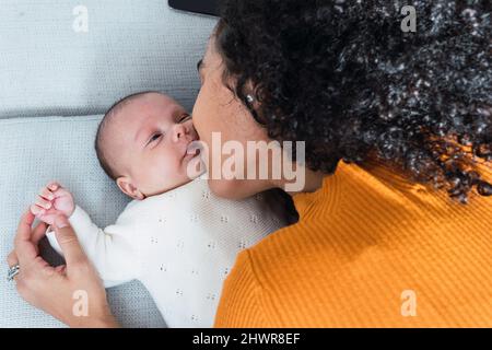 La madre bacia il figlio sdraiato sul divano nel soggiorno Foto Stock